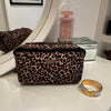 Mabel - Outlet leopard print makeup bag on a vanity with jewelry and perfumes.